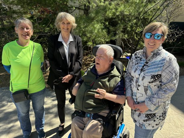 3 woman standing, Lorraine, Mayor Nancy Alcock, and Suzanne, and one man, Glen, seated in a wheelchair.