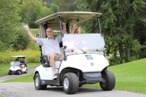 2 men in a golf cart raise their hands in the air in cheer.