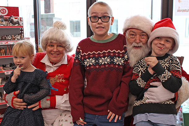 3 children sit in a toy store with Mrs Claus and Santa Claus.