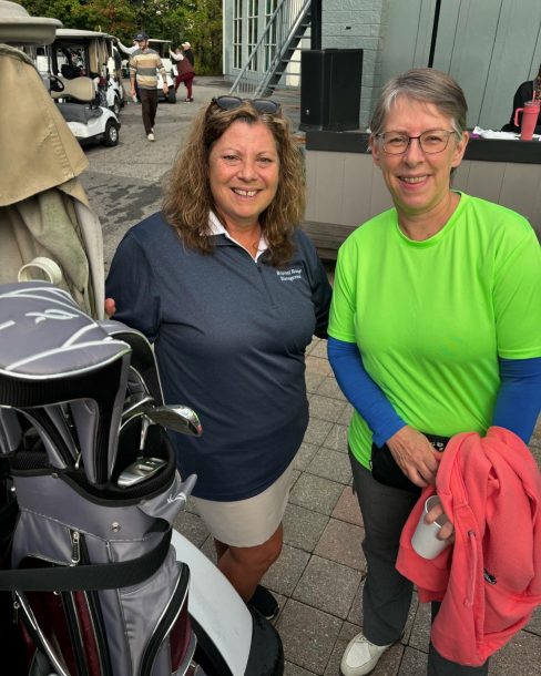 2 smiling women pose for a photo beside a golf cart.