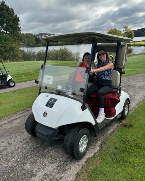 2 smiling women in a golf cart on a golf course.