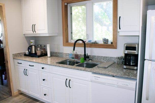 A view of a kitchen sink area in a bright kitchen with white cupboards.