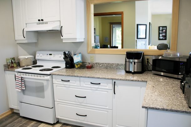 A view of a kitchen stove in a bright kitchen with white cupboards.