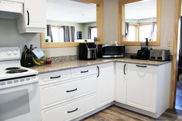 A view of a microwave on a kitchen counter. The wall behind the microwave is replaced by a pass-through window into a living room area.